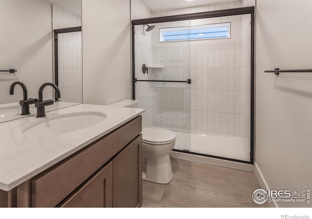 full bathroom featuring vanity, toilet, wood finished floors, and a stall shower