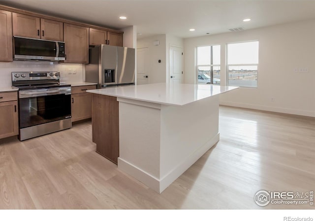 kitchen featuring light wood finished floors, tasteful backsplash, a center island, appliances with stainless steel finishes, and light countertops