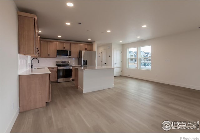 kitchen featuring a kitchen island, recessed lighting, appliances with stainless steel finishes, light wood-style floors, and a sink