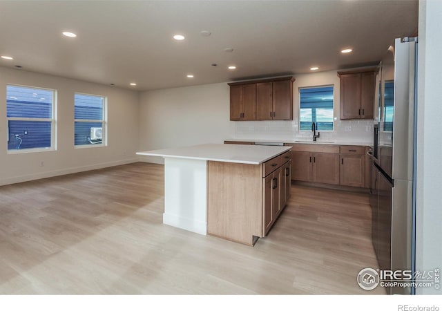 kitchen with a sink, backsplash, light wood finished floors, and a center island