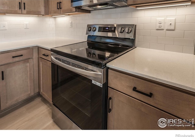 kitchen featuring light wood-style flooring, decorative backsplash, wall chimney exhaust hood, light countertops, and stainless steel electric range oven