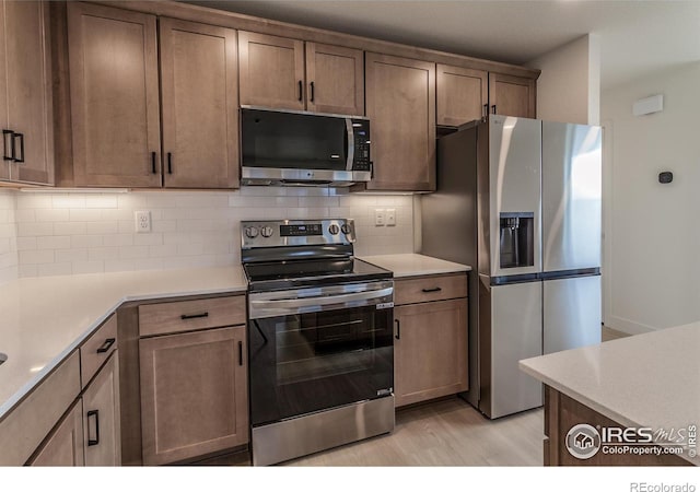 kitchen with light wood-type flooring, appliances with stainless steel finishes, decorative backsplash, and light countertops