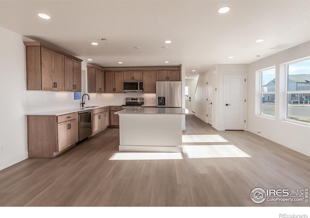 kitchen with a kitchen island, light wood-style flooring, a sink, light countertops, and appliances with stainless steel finishes