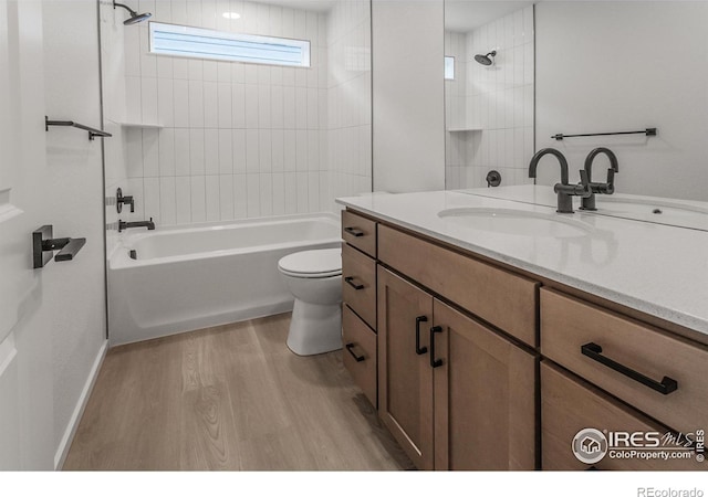 bathroom featuring vanity, wood finished floors, baseboards, bathing tub / shower combination, and toilet