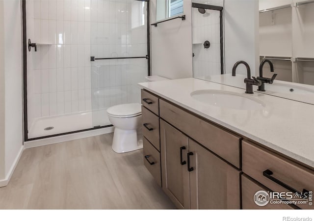 bathroom with vanity, toilet, wood finished floors, and tiled shower