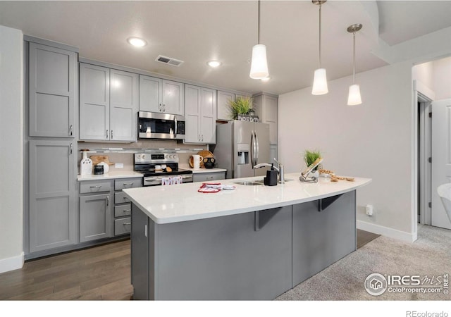 kitchen featuring visible vents, gray cabinetry, light countertops, stainless steel appliances, and a kitchen island with sink