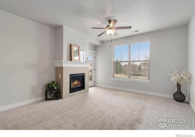 unfurnished living room with a tiled fireplace, visible vents, baseboards, and carpet floors