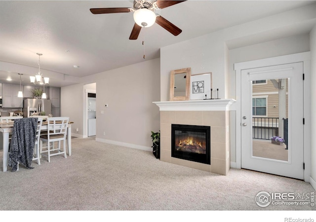 living area featuring ceiling fan with notable chandelier, a fireplace, baseboards, and light carpet