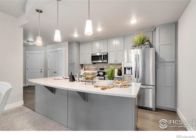 kitchen with gray cabinetry, stainless steel appliances, light countertops, and a kitchen breakfast bar