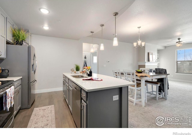 kitchen with a center island with sink, gray cabinetry, light countertops, appliances with stainless steel finishes, and light wood-type flooring