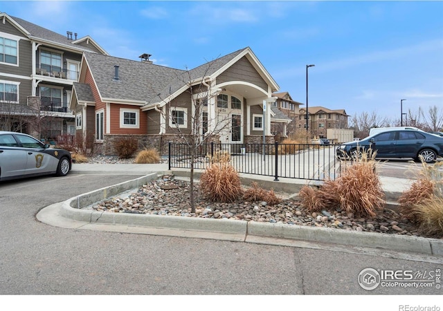 view of property featuring stone siding, fence, a residential view, uncovered parking, and a shingled roof