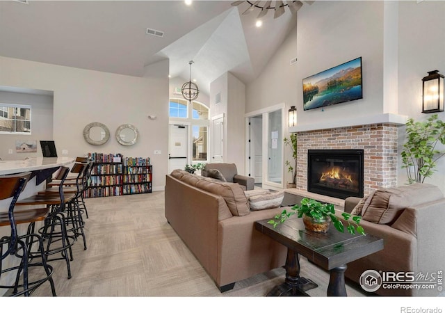 living room with visible vents, high vaulted ceiling, a brick fireplace, and light colored carpet