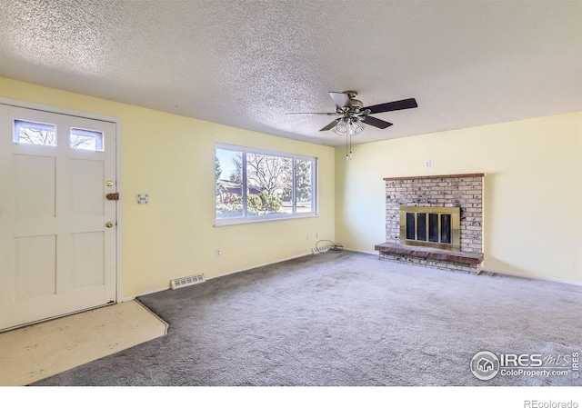 unfurnished living room with visible vents, a textured ceiling, carpet floors, a brick fireplace, and ceiling fan