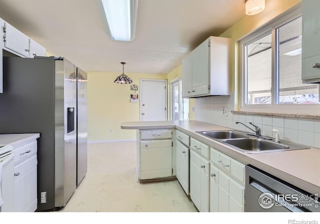 kitchen featuring backsplash, light countertops, a peninsula, stainless steel appliances, and a sink