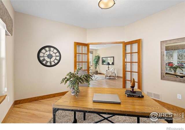 office space with light wood-style floors, visible vents, and baseboards