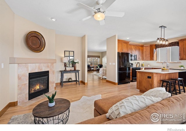 living area featuring baseboards, a fireplace, recessed lighting, ceiling fan, and light wood-style floors