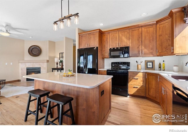 kitchen featuring a center island, brown cabinets, a tile fireplace, light wood-style flooring, and black appliances