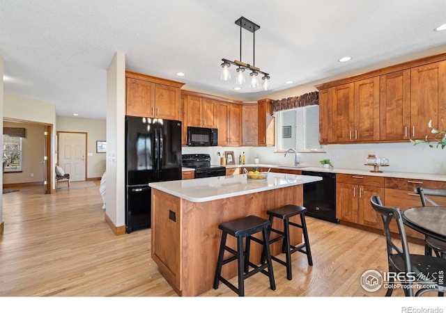 kitchen with black appliances, light wood-style flooring, a sink, a kitchen island, and light countertops