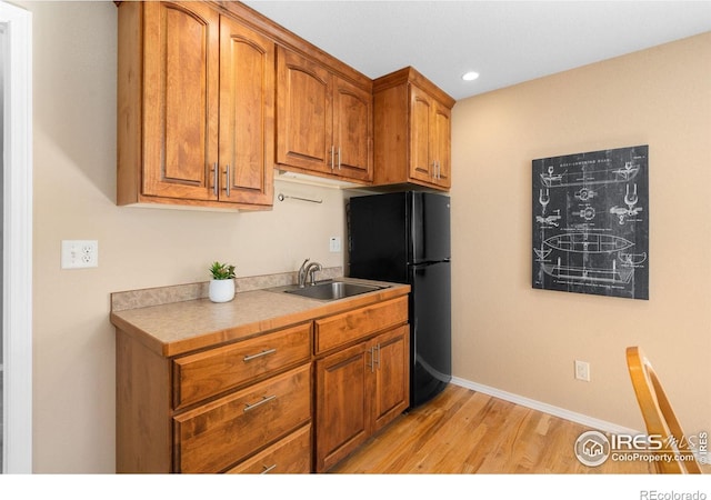 kitchen featuring light wood-style flooring, freestanding refrigerator, a sink, light countertops, and brown cabinets