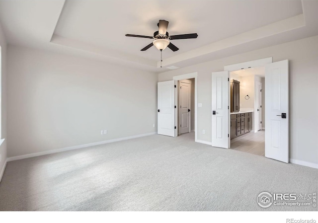1685 Crystalline Dr, Windsor, CO 80550 - unfurnished bedroom featuring baseboards, connected bathroom, a tray ceiling, ceiling fan, and light colored carpet