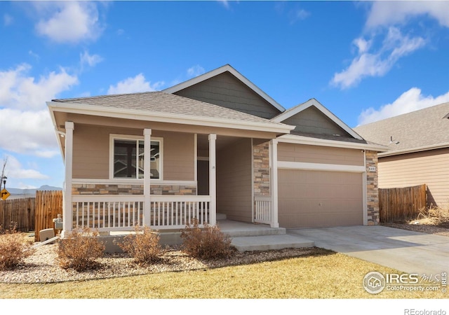 single story home with stone siding, a porch, concrete driveway, and fence