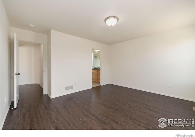 unfurnished room featuring visible vents, baseboards, and dark wood finished floors