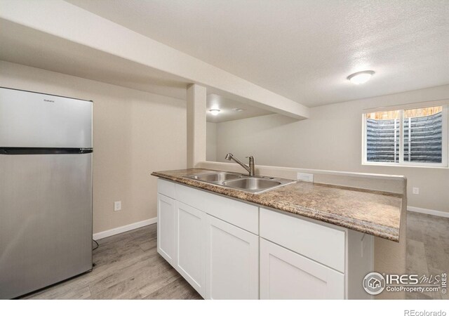 kitchen with white cabinets, light wood-type flooring, freestanding refrigerator, and a sink