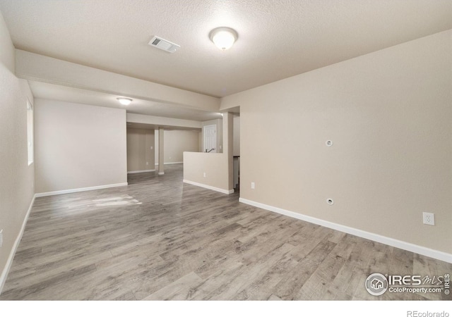 empty room featuring a textured ceiling, wood finished floors, visible vents, and baseboards