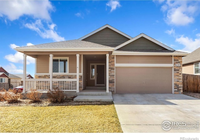 view of front of home with driveway, stone siding, covered porch, a shingled roof, and a garage