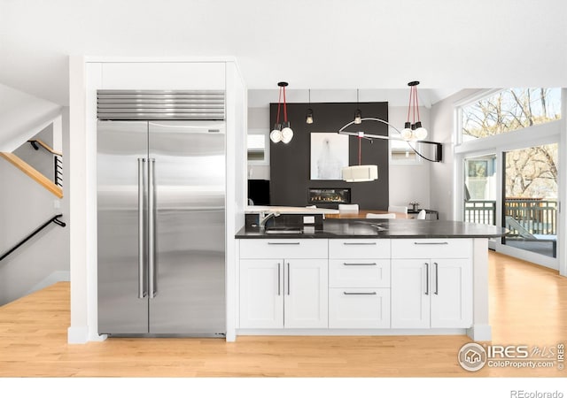 kitchen with stainless steel built in refrigerator, white cabinets, light wood finished floors, and dark countertops