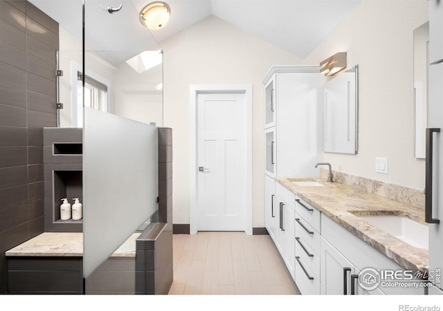 bathroom with lofted ceiling, walk in shower, double vanity, and a sink