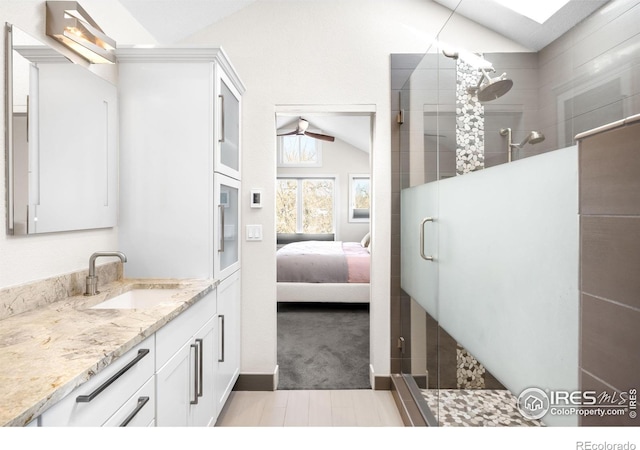 ensuite bathroom featuring tiled shower, vanity, and lofted ceiling