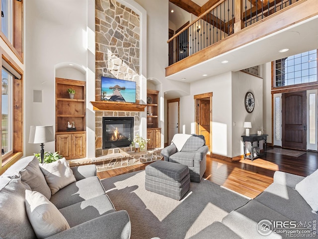 living room featuring built in features, a stone fireplace, a high ceiling, wood finished floors, and arched walkways