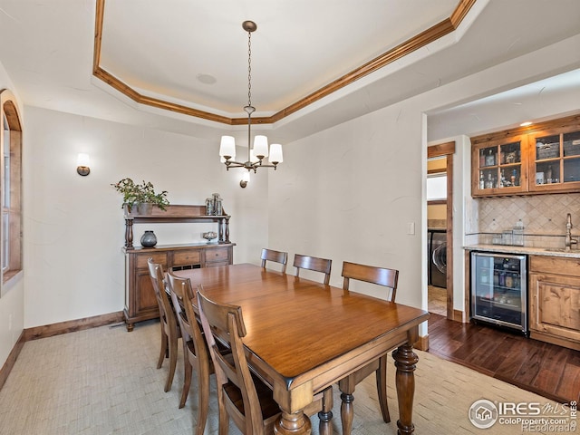 dining room with crown molding, beverage cooler, washer / dryer, an inviting chandelier, and a raised ceiling