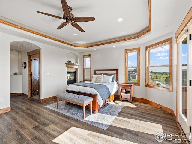 bedroom featuring a glass covered fireplace, baseboards, a raised ceiling, and wood finished floors