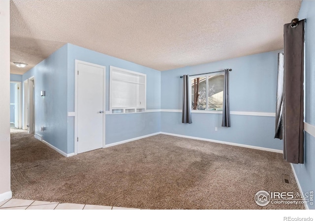 tiled empty room featuring baseboards, carpet, and a textured ceiling