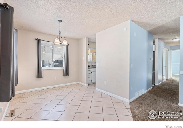 spare room with baseboards, light tile patterned flooring, a sink, a textured ceiling, and a chandelier