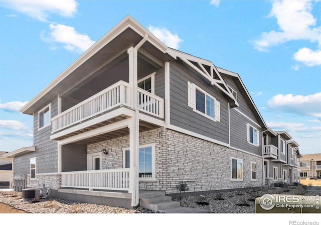 view of side of home with central air condition unit, a balcony, covered porch, and stone siding