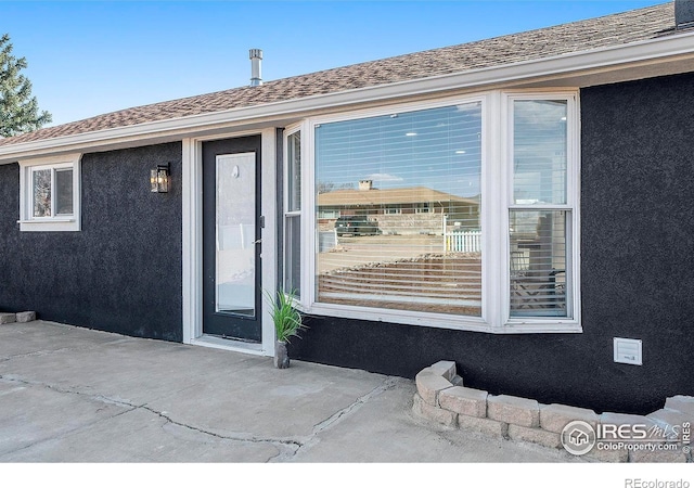 entrance to property featuring stucco siding and roof with shingles