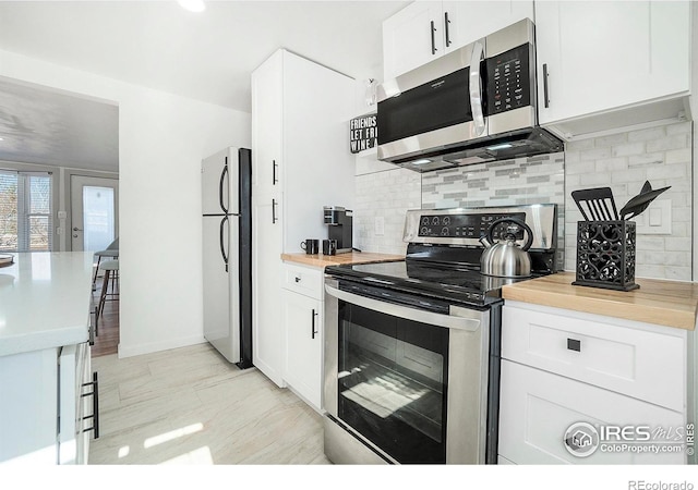 kitchen featuring wooden counters, decorative backsplash, appliances with stainless steel finishes, and white cabinetry