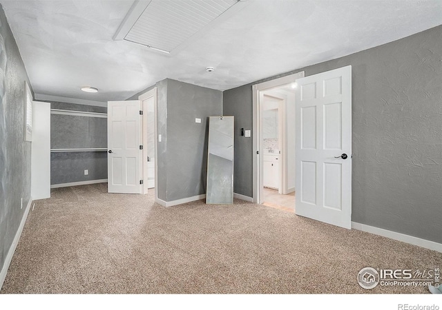 unfurnished bedroom with a spacious closet, carpet flooring, a textured wall, and baseboards