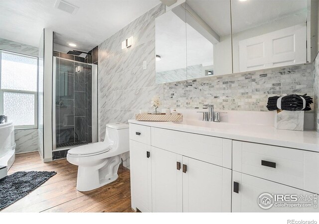 full bath with toilet, a stall shower, wood finished floors, tile walls, and vanity