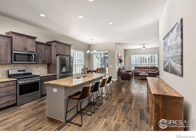 kitchen with backsplash, open floor plan, appliances with stainless steel finishes, a kitchen breakfast bar, and a sink