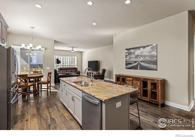 kitchen with a sink, stainless steel appliances, an island with sink, and dark wood-style flooring