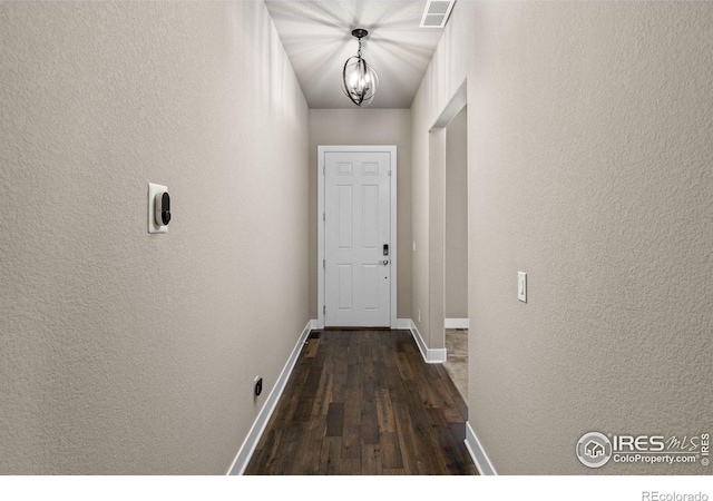 doorway to outside with visible vents, baseboards, an inviting chandelier, a textured wall, and dark wood-style floors