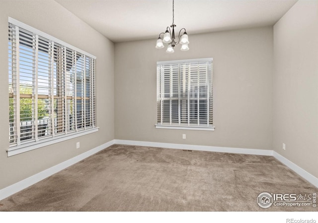 carpeted empty room featuring a chandelier and baseboards