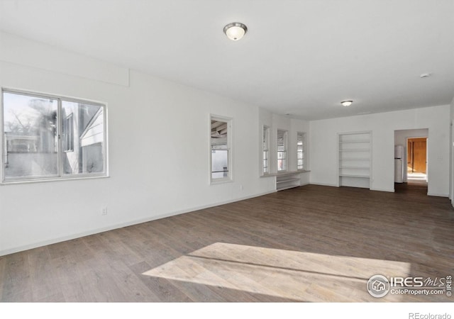 unfurnished living room with baseboards, built in shelves, and wood finished floors