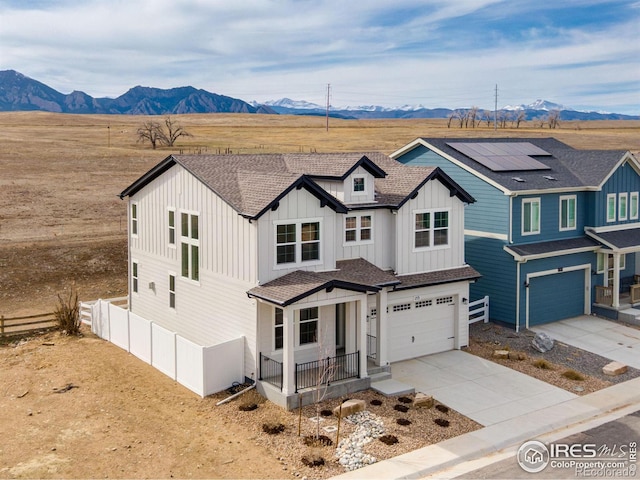 view of front facade with board and batten siding, fence, roof mounted solar panels, driveway, and a mountain view