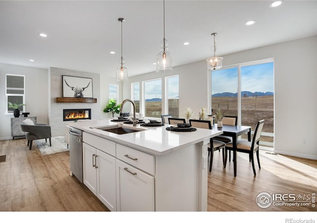 kitchen with light wood finished floors, a sink, stainless steel dishwasher, a mountain view, and a large fireplace