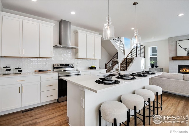 kitchen featuring visible vents, a breakfast bar, stainless steel range with electric stovetop, open floor plan, and wall chimney range hood